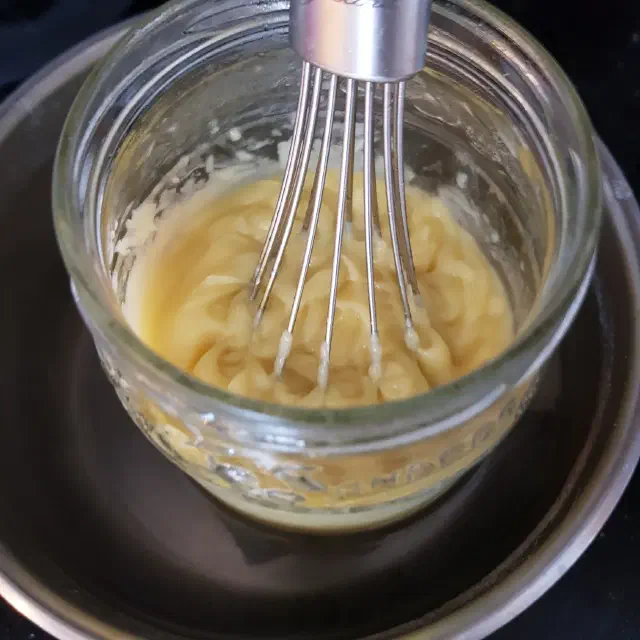 Pâte à savon jaune contenue dans un bocal en verre, un fouet est planté verticalement dedans.